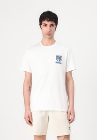 Balta medvilninė marškinėliai su mėlyna ir žalia stilizuoto gyvūno veido grafika kairėje krūtinės pusėje. Trumpi rankovės, apvalaus kaklo dizainas.