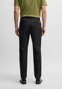 Black trousers with a straight cut, featuring back pockets and a smooth texture, worn with a green shirt and black shoes.