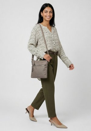 Woman wearing patterned blouse and olive trousers, carrying grey crossbody bag, walking with beige slingback heels against plain background.