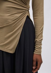 Langemouwtop van ribbelbeige stof met gedraaide zijdetail, gecombineerd met een zwierige zwarte rok. Zachte textuur met subtiele draping.