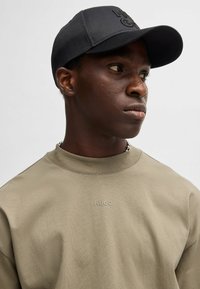 Schwarze Kappe mit geprägtem Logo, beiger Sweatshirt mit dezentem Logo auf der Brust, glattes Material, Rundhalsausschnitt, schlichtes Design.