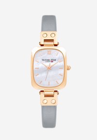Montre rectangulaire avec un boîtier en métal rose doré, un cadran en nacre, un bracelet en cuir texturé gris et le chiffre romain XII en haut.