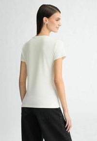 Lichtgrijs shirt met korte mouwen, ronde hals, een getailleerd ontwerp en een soepele textuur. Draag het met zwarte jeans met versieringen aan de zijkanten.