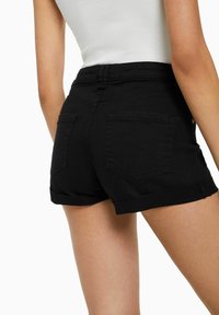 Shorts en denim noir avec un ourlet roulé, dotés de deux poches arrière et d'une taille ajustée. La texture est lisse avec une légère élasticité.