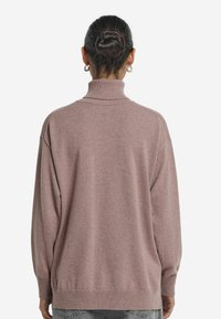 Osoba z ciemnymi włosami związanymi w kok, nosząca kolczyki w kształcie kół oraz fioletowy sweter z golfem, widoczna z tyłu na białym tle.