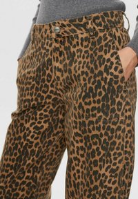 Hlače s leopardjim potiskom v rjavi in črni denim tkanini s stranskimi žepi. Značilnost je kovinski gumb za zapiranje in vidni šivi.
