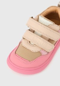 Ροζ και μπεζ παιδικό αθλητικό παπο ύτσι με διπλούς ιμάντες βέλκρο και κειμενική υφή στην περιοχή των δαχτύλων, πάνω σε λευκό φόντο.