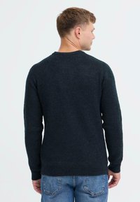 Tume roheline soonilise mustriga sviiter pikkade varrukatega ja ümmarguse kaelusega, millel on tekstuuriga kudum ja kitsad mansetid. Tagaplaan.