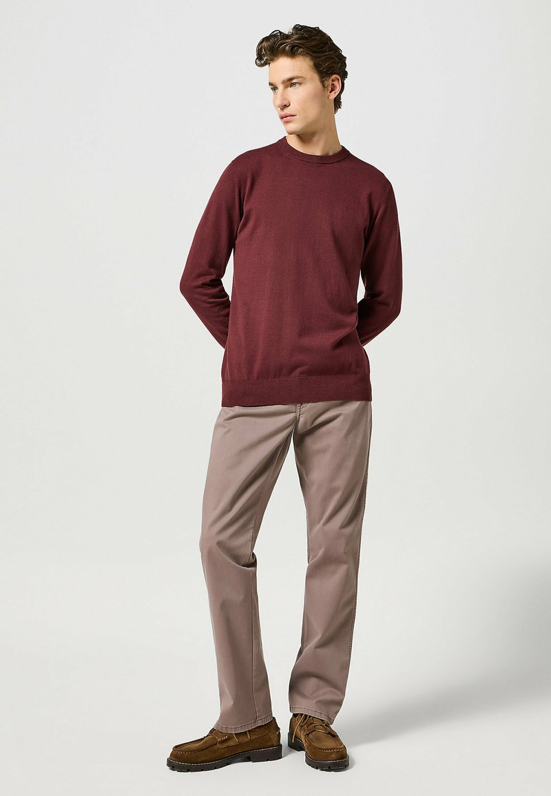 Maglione a maglia borgogna con scollo rotondo, abbinato a pantaloni beige e scarpe in suede marrone, caratterizzato da una vestibilità rilassata e una consistenza morbida.