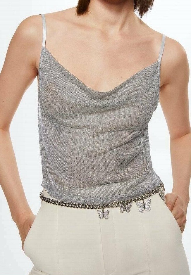 Haut sans manches métallique argenté à fines bretelles, associé à un pantalon crème taille haute et une ceinture chaîne ornée de breloques papillons.