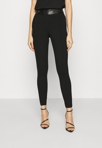 Černé přizpůsobené kalhoty s vysokým pasem a lesklým černým páskem. Hladká tkanina a elegantní design. V kombinaci s černými sandály na vysokém podpatku.