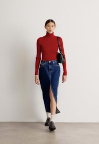 Rdeča prilegajoča se turtleneck pulover s visokim ovratnikom, krilo iz denima z visokim pasom in stranskim razporkom, črna torbica in črne loafer čevlje z belimi nogavicami.