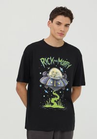 T-shirt in cotone nero con una grafica colorata di un'astronave, con personaggi all'interno, e una melma verde sul fondo. Collo rotondo, maniche corte.