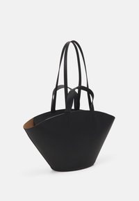 Sac cabas en cuir noir avec une base large unique, des côtés allongés et deux anses plates. L'intérieur présente une doublure marron contrastante.