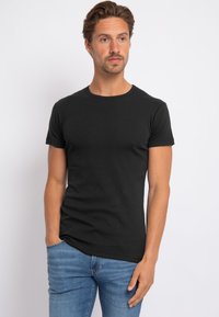 Zwarte t-shirt met ronde hals van katoen, met korte mouwen en een strakke pasvorm. Gepaard met lichtblauwe jeans. Eenvoudig ontwerp.