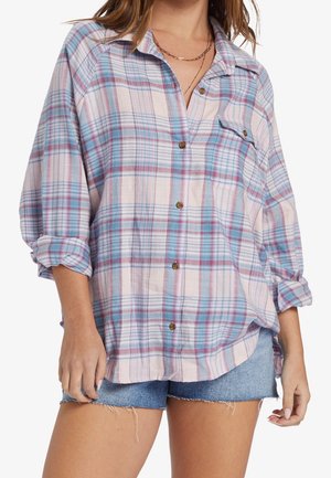 Woman wearing a loose pastel blue and pink plaid button-up shirt with rolled sleeves and denim shorts, showing upper body and mid-thigh.