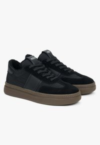Czarne sneakersy z zamszową i nylonową cholewką, z okrągłymi sznurowadłami, masywną brązową gumową podeszwą oraz akcentami logo na języku.