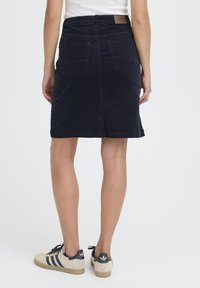 Mornarsko modra kordna krila z zadnjimi žepi, ravnim krojem in robom nad kolenom. V kombinaciji z bež supergami z črnimi črtami.