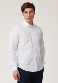 Camisa de manga larga blanca con un patrón azul claro de pequeños perros, cuello abotonado y un único bolsillo en el pecho con un acento aqua.