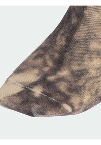 Brūna un bēša rakstaina zeķe ar ribveida struktūru; tai ir smaili pēdas gali un bezšuvju dizains. Viegls, mīksts materiāls.