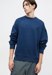 Marineblaue Sweatshirt mit lockerer Passform, rundem Halsausschnitt, gerippten Bündchen und Saum. Mit einem dezenten Logo auf der Brust und weichem Material.