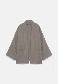 Veste grise ample à ouverture frontale, manches larges et deux poches devant, en tissu léger texturé.