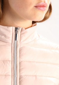 Hellrosa gesteppte Steppjacke mit hohem Kragen. Verfügt über einen Metallreißverschluss und eine horizontale Steppstruktur, die ein glattes Erscheinungsbild bietet.