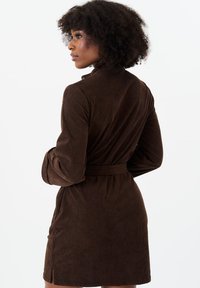 Brown corduroy wrap dress with a belted waist, long sleeves, and a split detail on the skirt. Features vertical ribbing texture.