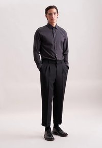 Donkergrijs shirt met lange mouwen en een button-down kraag, gecombineerd met formele zwarte geplooide broek. Zwarte leren schoenen maken de look compleet.