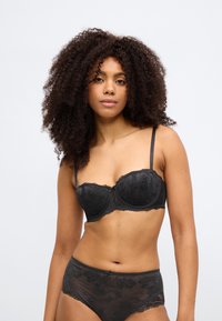 Σετ εσώρουχα από μαύρη δαντέλα με στητό σουτιέν balconette και σλιπ ψηλόμεσο. Διαθέτει λουλουδάτα σχέδια και λεπτές ρυθμιζόμενες τιράντες.