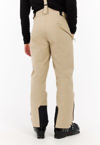 Beige skibroek met verstelbare banden, zwarte accenten bij de onderbenen en ritszakken, ontworpen voor optimale prestaties in de wintersport.