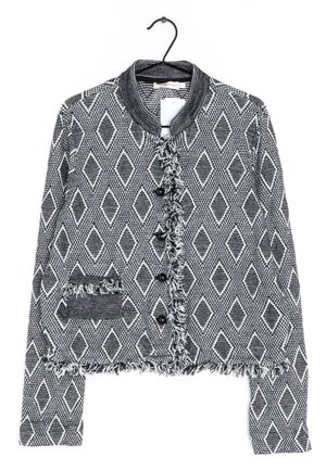 Veste à motif noir et blanc avec des formes en losange, bordure à franges, boutons noirs et petite poche avant, suspendue à un cintre noir.