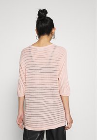 Maglione lavorato a maglia di un delicato rosa chiaro con motivo a rete e righe orizzontali. Presenta maniche a tre quarti e un ampio scollo.