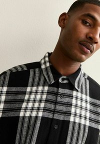 Camicia a quadri in bianco e nero con colletto button-down, texture morbida e pattern a contrasto con linee orizzontali e verticali prominenti.