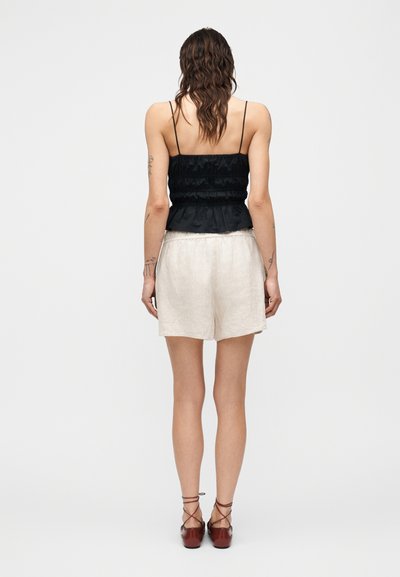 Μαύρο τοπ με ρούαγ τσακίσματα και λεπτές τιράντες, συνδυασμένο με ανοιχτό μπεζ σορτς από λινό, με άνετη εφαρμογή. Το σύνολο ολοκληρώνουν καστανά παπούτσια με λουράκια.