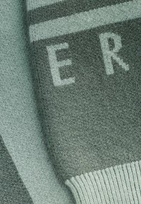 Žakardo audinys žalsvais atspalviais su tekstūruota paviršiumi. Sukurtas drąsiais baltais užrašais ir susiraukšlėjusia kraštine. Dryžuotas dizainas prideda kontrasto.