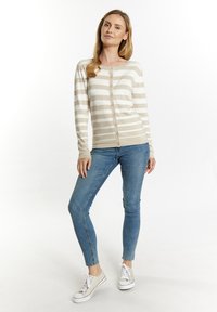 Beige und cremfarbener gestreifter Cardigan mit Knopfleiste, langen Ärmeln und einer weichen Textur, kombiniert mit blauen Skinny Jeans und hellen Sneakers.