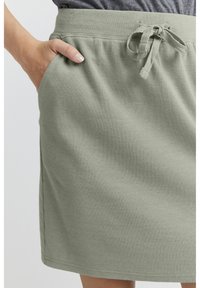 Fustă ribbed de culoare verde deschis, cu un tiv cu șnur și buzunare laterale. Textura este moale și ușor elastică, potrivită pentru o ținută casual.