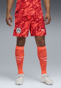 Shorts de soccer rayés rouge et orange avec le logo BVB 09, accompagnés de chaussettes orange montantes avec un design texturé et des accents blancs.