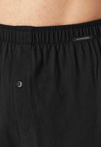 Boxer neri in cotone con un morbido elastico in vita, chiusura a bottoni e una piccola etichetta con logo sulla cintura. Texture liscia e vestibilità classica.