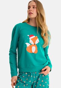 Haut à manches longues turquoise avec un renard orange stylisé portant un chapeau de Santa. Associé à un pantalon vert orné de motifs de renards et de fleurs.