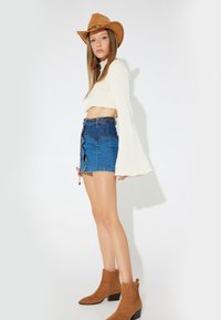 Krämfärgad texturerad crop top, högmidjad denim minikjol med slits och dragsnörning, samt tanfärgade mocka ankelskor.