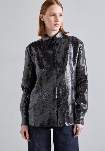 Chemise noire à paillettes avec un col, des manches longues et une coupe légèrement ample, associée à un pantalon en denim foncé.