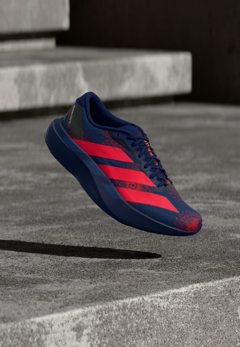 Marineblauer und leuchtend roter Laufschuh, der über Betonstufen schwebt und florale Muster sowie kräftige Streifen an der Seite zeigt.