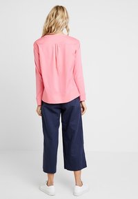Felpa rosa chiaro con piega sul retro, abbinata a pantaloni navy a culotte. L'outfit presenta una vestibilità rilassata e scarpe da ginnastica bianche.
