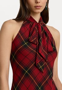 Top halter roșu cu carouri, cu un decolteu în formă de fundă, având accente negre și galbene. Textură netedă, cu un design aderent și umeri deschiși.