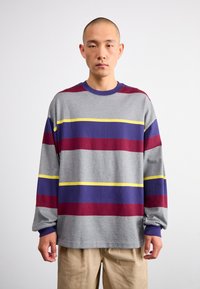 Pelēka garām piedurknēm krekls ar horizontālām svītrām bordo, violetā un dzeltenā krāsā. Mīksta tekstūra, brīvā fitā, un ribotas piedurknes.