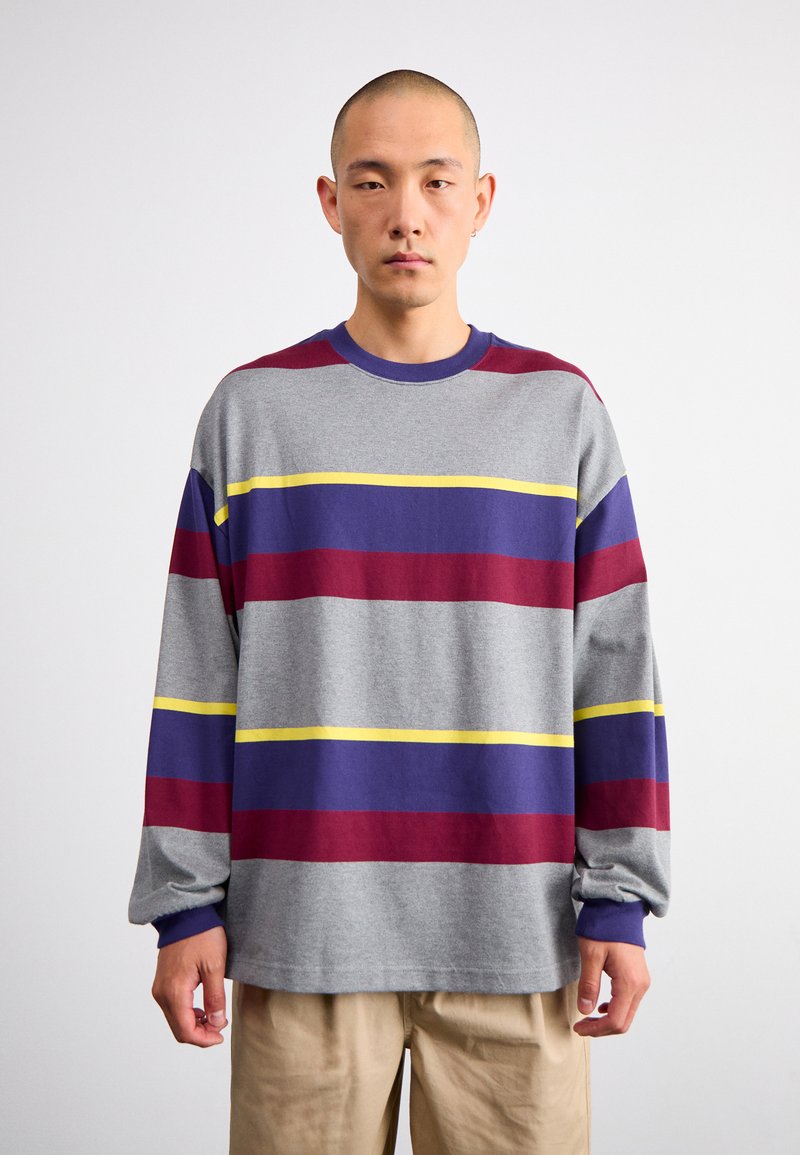 Pelēka garām piedurknēm krekls ar horizontālām svītrām bordo, violetā un dzeltenā krāsā. Mīksta tekstūra, brīvā fitā, un ribotas piedurknes.