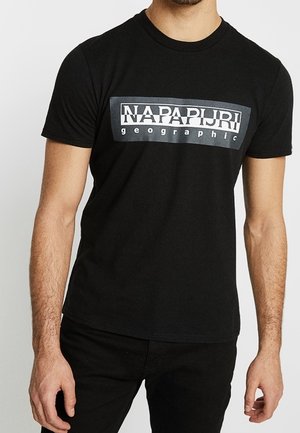 Mand iført en sort kortærmet T-shirt med et rektangulært logo med teksten "NAPAPIJRI geographic" i hvid og grå på brystet.