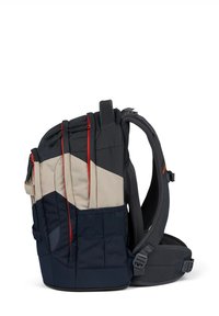 Sac à dos en tissu durable bleu marine et beige avec des accents rouges. Il possède des bretelles rembourrées, plusieurs poches zippées et une forme structurée.